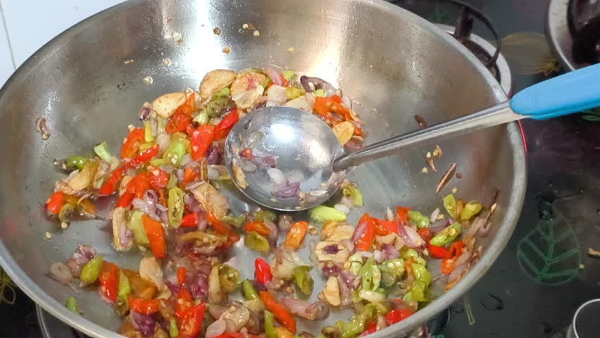 Chopped garlic, shallots, and chili sizzle in a stainless steel wok, creating a fragrant base. Oyster sauce and other seasonings are added, transforming the simple ingredients into a flavorful mix.
