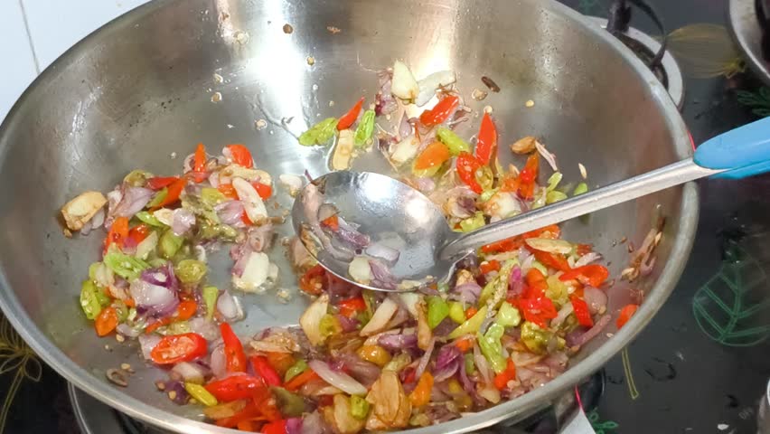Chopped garlic, shallots, and chili sizzle in a stainless steel wok, creating a fragrant base. Oyster sauce and other seasonings are added, transforming the simple ingredients into a flavorful mix.