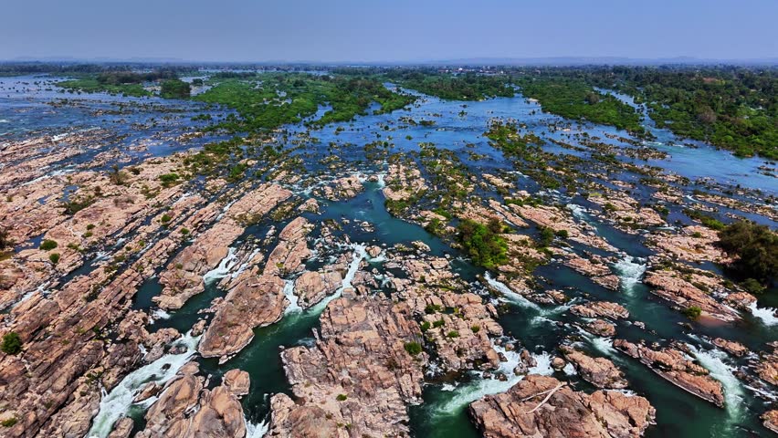 Aerial view of the Mekong River flowing through rocky rapids and lush green islets in Don Det, Laos, illustrating the river’s powerful currents, scattered vegetation, and vast natural expanse