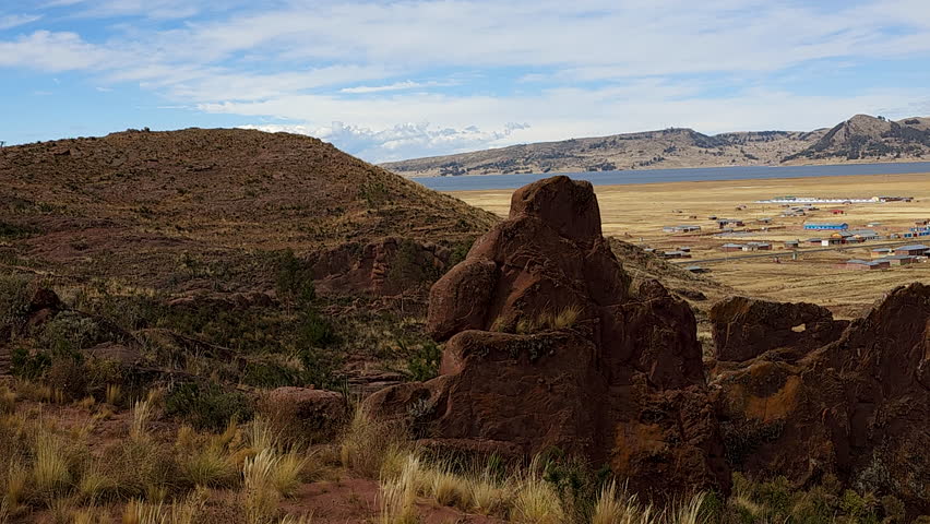 A breathtaking panoramic view from a mountaintop near the Aramu Muru archaeological site in Peru, with the vast landscape, Lake Titicaca, and distant mountains