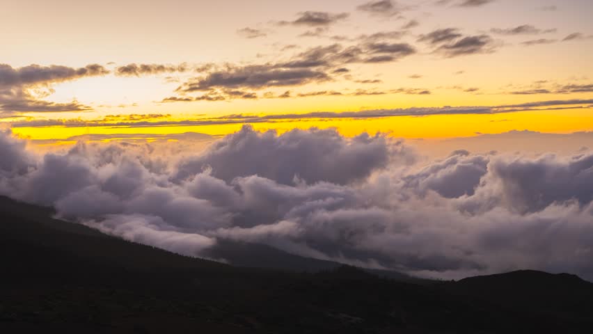 Timelapse of twilight after sunset at Teide National Park, red-yellow sky fading, cloud waves rising like ocean tides toward volcano base, darkening sky over volcanic landscape

