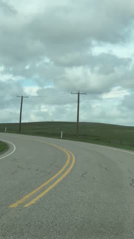 Driving down the highway during summertime daylight in Alberta, Canada, scenic road view from driver’s perspective surrounded by open fields and cloudy sky