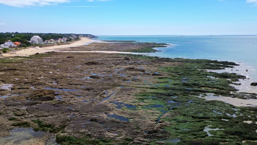 Forward drone movement over the Plage de Bonne-Source rocky shore with shallow tidal streams near the open sea, Loire-Atlantique, France.