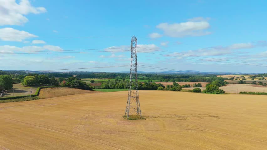 Drone orbit movement of a UK Electricity Pylon, Aerial view of industrial utility structure with surrounding farmland and fields.