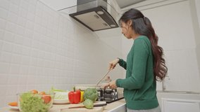 Young woman cooking in modern kitchen with fresh ingredients, preparing healthy meal with vegetables, using frying pan and utensils on stovetop - Powered by Shutterstock - Get 15% off with code: PIKWIZARD15