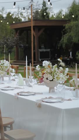 Wedding decor, dinner. Decorated dining table with vase and bouquet of flowers. Outdoor event. No food. Flower arrangement with fresh bouquet for wedding event or function. Vertical video.