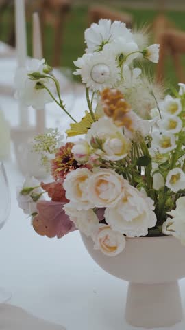 Wedding dinner table setting. Flowers in a vase on the dining table, close-up of a bouquet of pastel fresh flowers outdoors. Vertical video Flower arrangement on the table, slow motion. Wedding