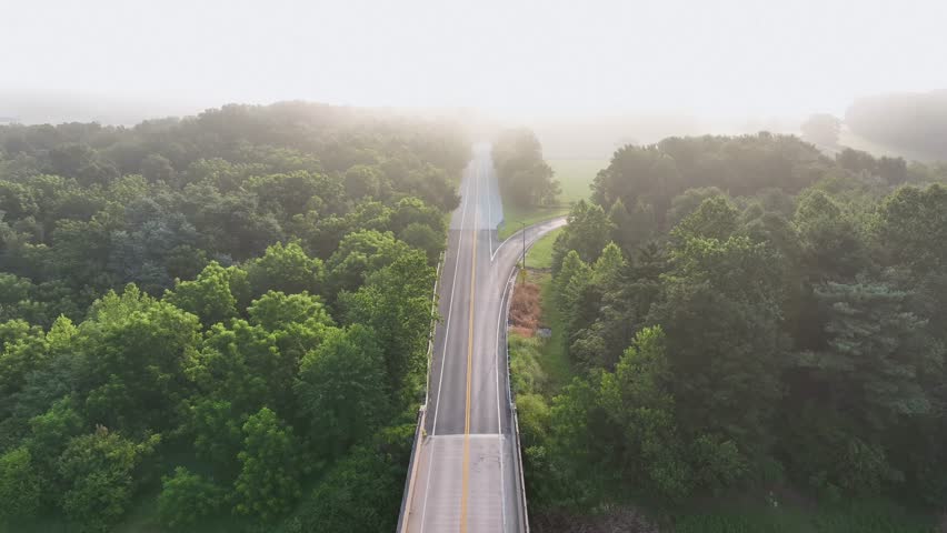 Bright sun rays in forest landscape with bridge of America. Aerial backwards wide shot. Empty highway road in suburb of town. Natural scene at sunrise.