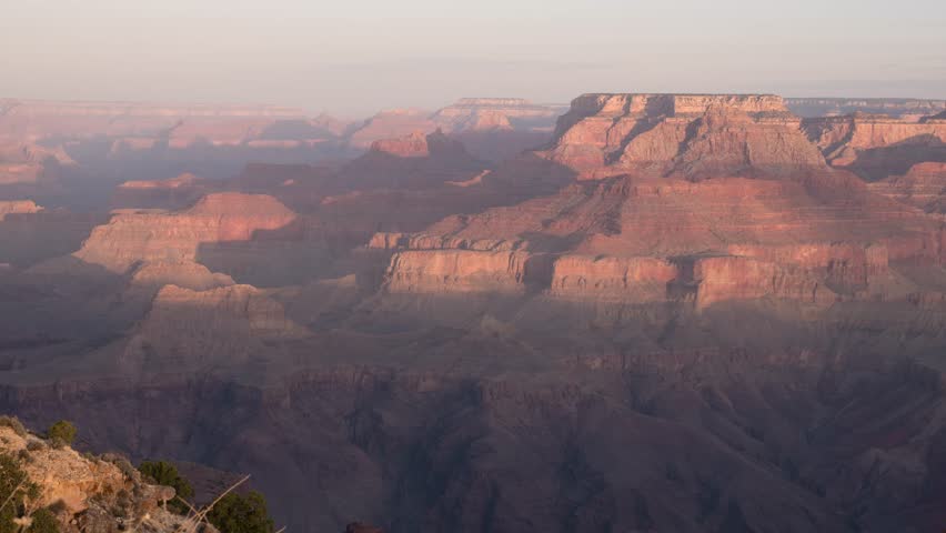 Aerial drone shot of Grand Canyon showcasing panoramic rock formations bathed in sunlight with stunning geological features and vast desert landscape in Arizona, captured in time lapse