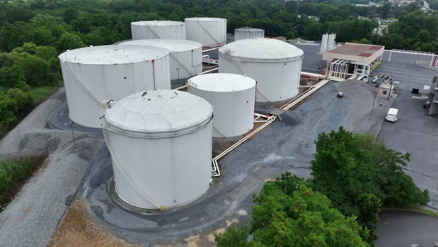 White rusty storage tanks for fuel at terminal in American town. Pipelines connecting circular silos. Aerial flyover shot. Industrial factory in Harrisburg, America.