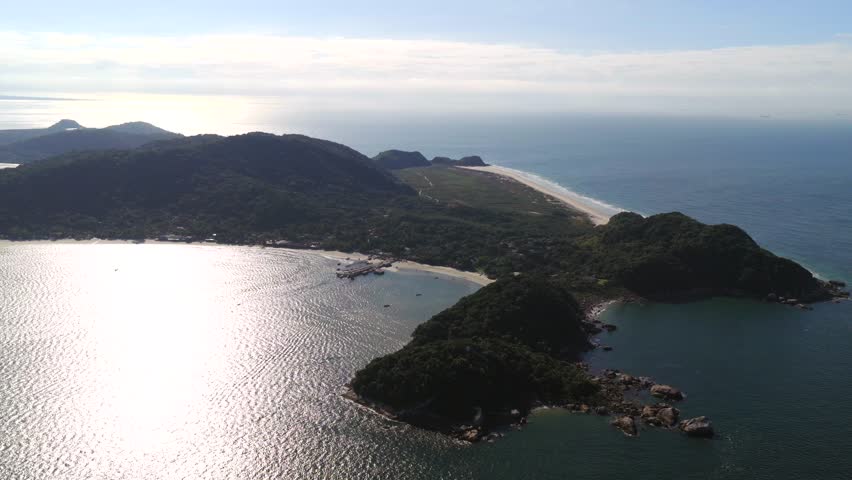 Aerial view of Ilha do Mel, Paraná coast, with beaches, forest, and rocky coastline under sunlight.