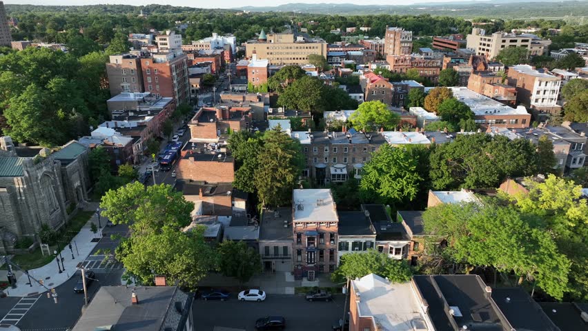 Aerial drone view of downtown Albany, New York. Historic brick buildings, leafy streets and low-rise architecture blend with modern office buildings, framed by green parks and distant hills.