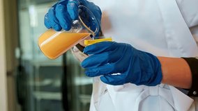 A close-up shot shows a scientist in a lab coat and blue gloves carefully pouring an orange liquid from a glass beaker for a medical or chemical research experiment. - Powered by Shutterstock - Get 15% off with code: PIKWIZARD15