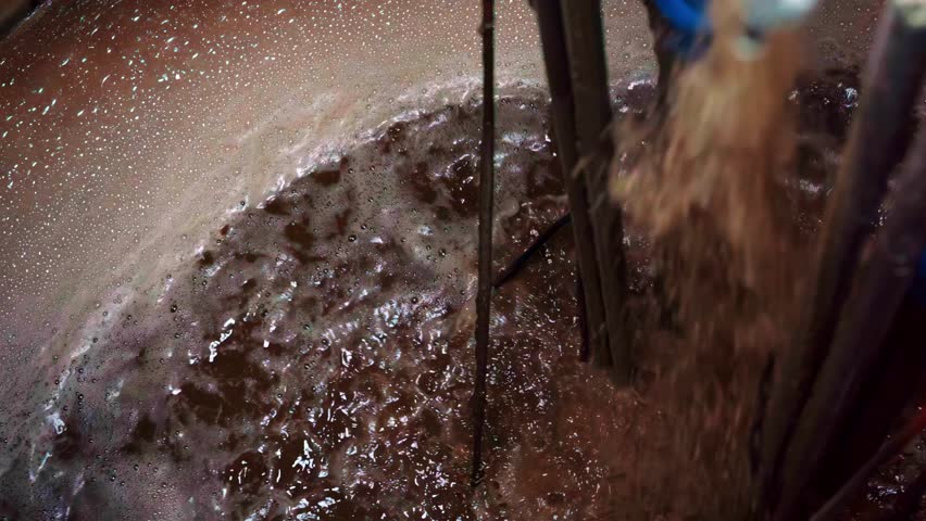 A close-up shot shows the industrial process of bubbling wastewater being aerated and cleaned in a large tank at a water treatment or purification plant.