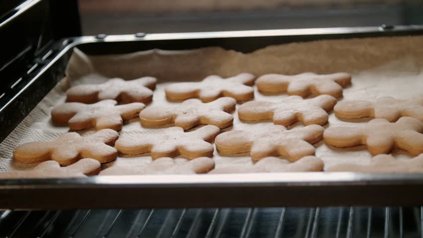 Freshly baked gingerbread bear cookies on a tray in the oven, sprinkled with sugar