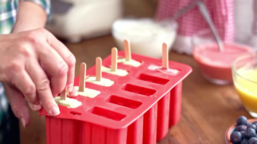 Close up of hands making homemade popsicles with fruit, yogurt, and orange juice