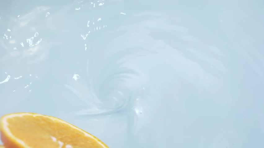 Closeup of an orange slice splashing into clear water with a swirling motion