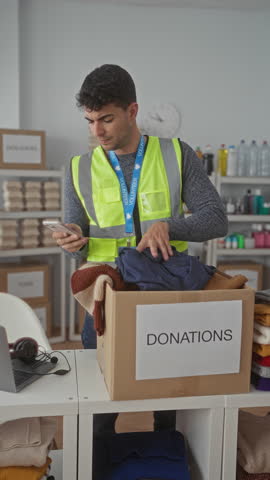 Man places clothes into a box while sorting at a warehouse with a hispanic young volunteer collecting donations for a male charity group.