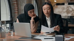 Two multiracial business women female colleagues employers multiethnic businesswomen Asian woman Muslim girl concentrated solving corporate work problem discuss with laptop document at office table - Powered by Shutterstock - Get 15% off with code: PIKWIZARD15