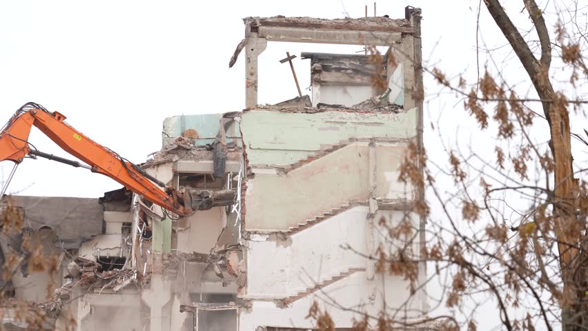 Excavator demolishes concrete building, creating dust and debris as it tears down the structure