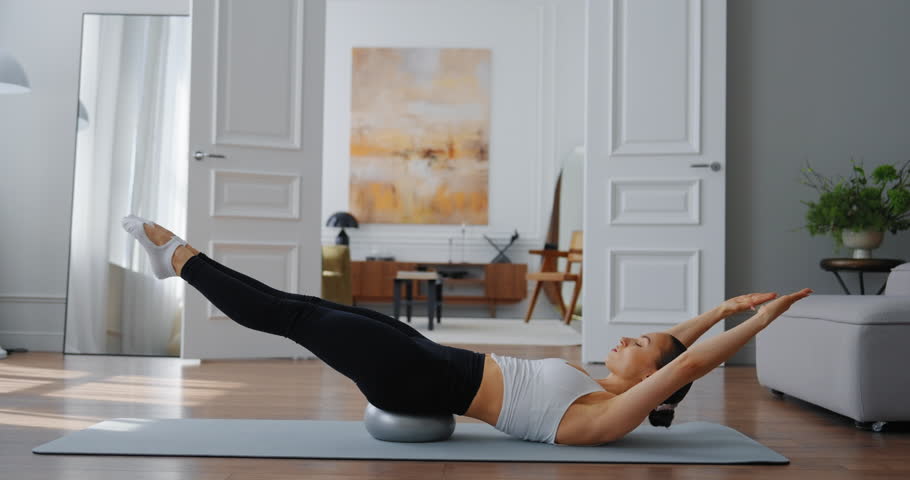 Woman practicing Pilates on exercise ball in modern living room with stylish decor and natural light