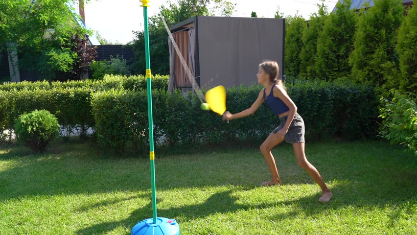 Girl plays tetherball in a sunny backyard with her dog, enjoying summer fun and exercise