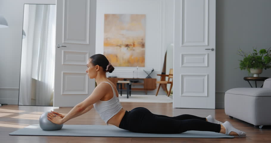 Woman practicing yoga with exercise ball in modern living room with bright natural light