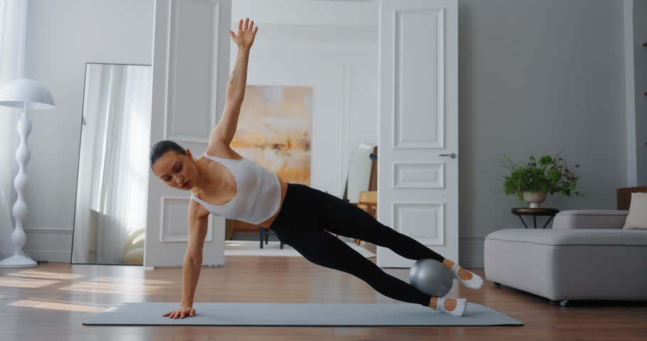 A Pilates-loving woman performs a dynamic exercise with a ball in a modern living room