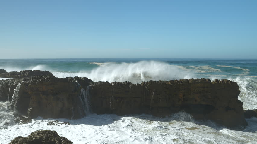 SLOW MOTION: Crashing of a big wave against dark shore rocks causes an immense explosion of white water and foam. Incredible power of the Atlantic Ocean creates dramatic scenes along Moroccan coast.