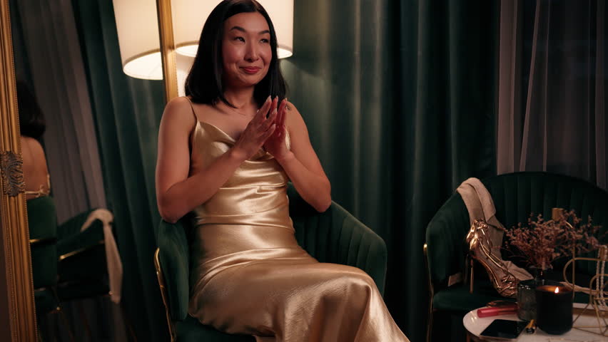 Portrait indoor happy smiling pensive dreaming thoughtful Asian woman beautiful in gold dress rub hands together in anticipation tap with fingers create idea Korean female Japanese Chinese lady dream