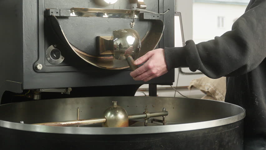 Unrecognizable man worker male hand pushing lever in roasted coffee machine opening flow falling beans cocoa grains mixing blending roasting in fabric small business preparing caffeine production