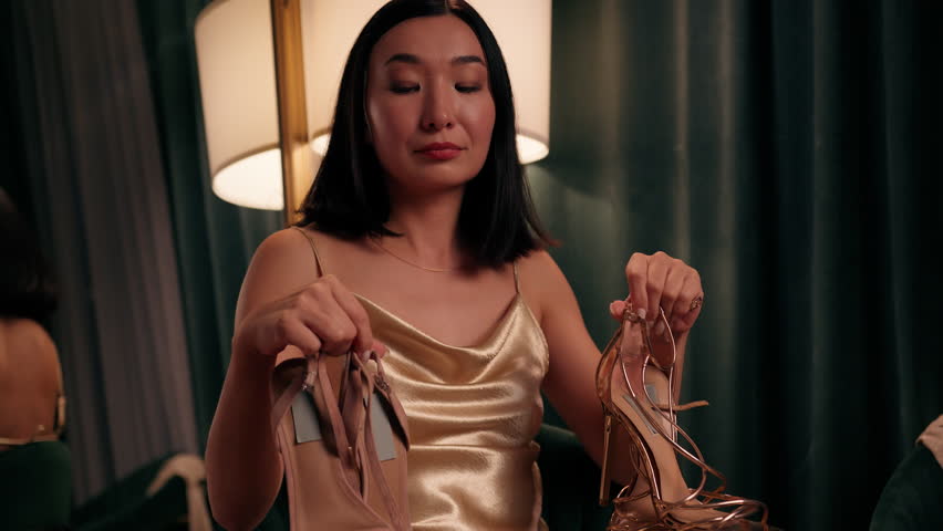 Asian woman Chinese female choosing between two pairs of shoes Korean lady Japanese model preparing to date party thinking hesitate deciding indoors stylish fashionable decision difficult variety