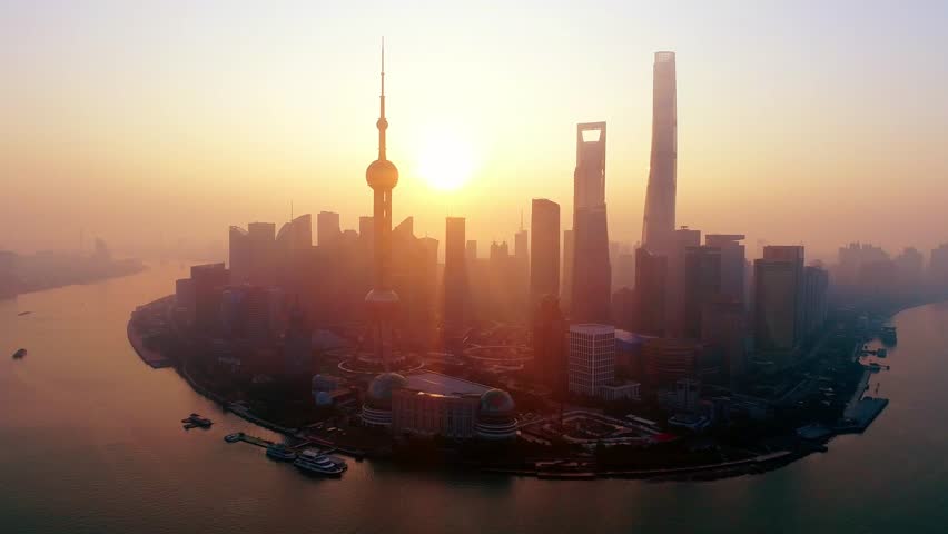 Shanghai. Aerial view of a city skyline during sunset, with a prominent Oriental Pearl Tower in the foreground. The cityscape is bathed in a warm, golden hue, suggesting either dawn or dusk.