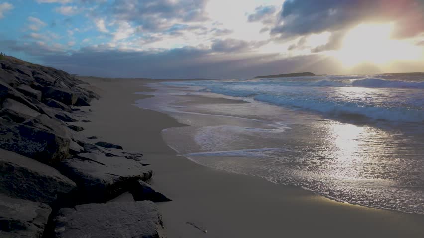 Footage with sound of incoming waves from the Pacific Ocean coming into a rocky shoreline at sunrise near the town of Warilla in the Illawarra region on the south coast of New South Wales, Australia.