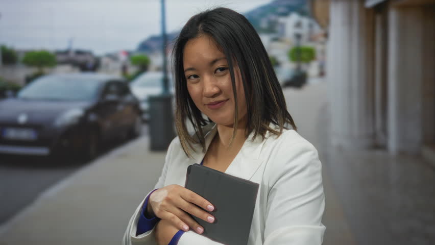 Woman in white jacket holding tablet extends hand on city street capturing a blend of urban connectivity with youthful energy and professional demeanor.