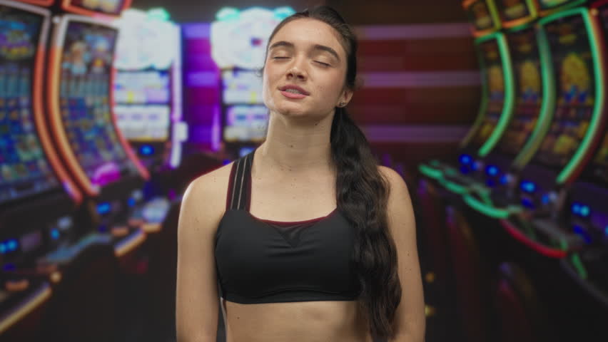 Woman with long hair standing with eyes closed and smiling softly before slot machine in casino; serenity.