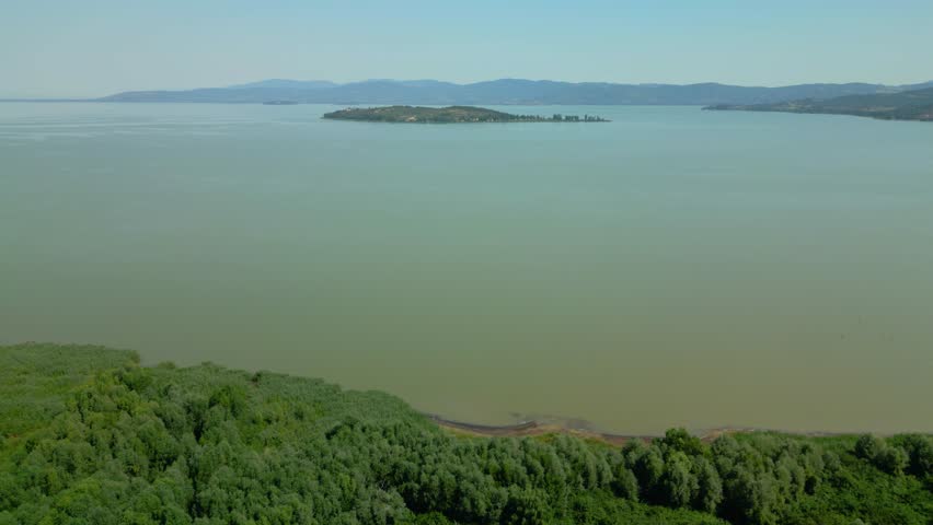 Aerial view showcasing the serene beauty of lake trasimeno, with isola maggiore prominently featured amidst the tranquil waters and bordered by vibrant, verdant vegetation