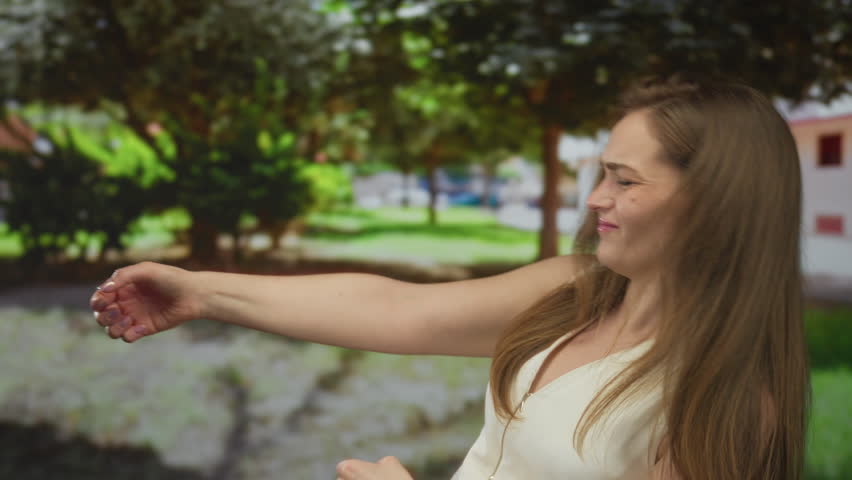 Young caucasian woman pulls an imaginary rope with outstretched arm among green trees in forest; determination.