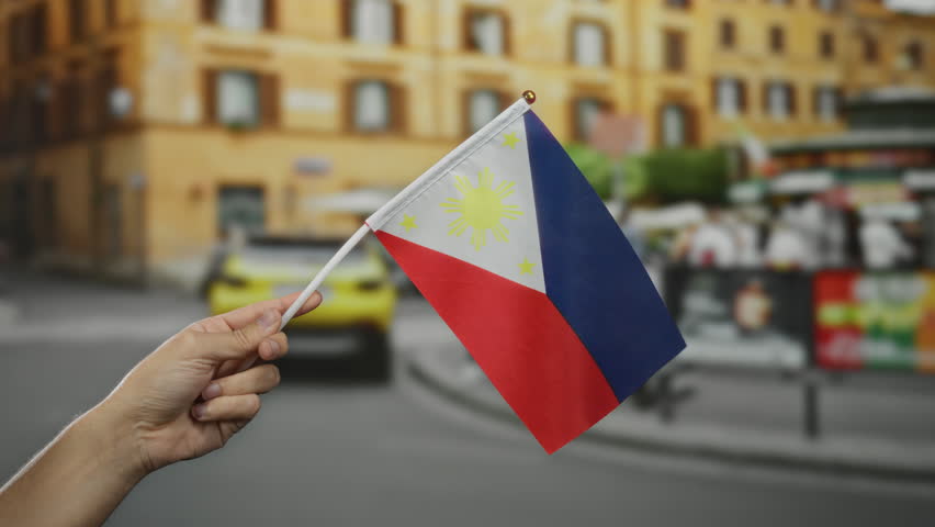 Hand holding philippine flag in a vibrant city street with blurred background, highlighting cultural pride and urban life.