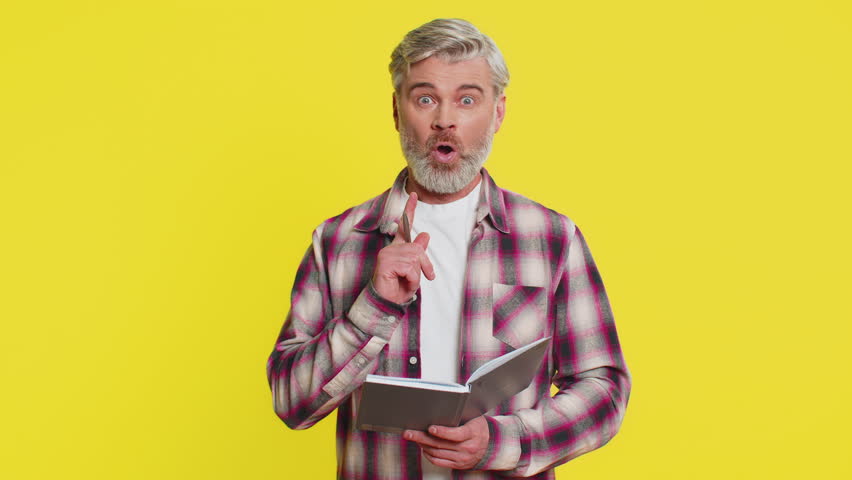 Thoughtful journalist Caucasian middle-aged man making notes, writing down thoughts with pen into notepad notebook diary, to do list, good idea. Mature old guy isolated on yellow background indoors