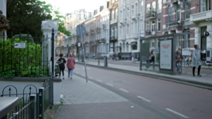 Blurry street scene with women walking along a european city sidewalk, showcasing defocused urban architecture and relaxed outdoor atmosphere under the soft bokeh light.