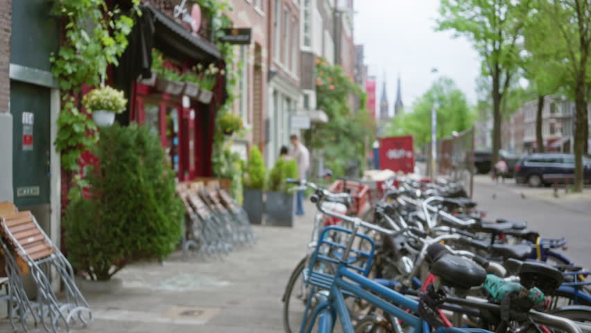Defocused bicycles lined along a vibrant amsterdam street with blurred pedestrians and colorful buildings creating a classic dutch urban setting.