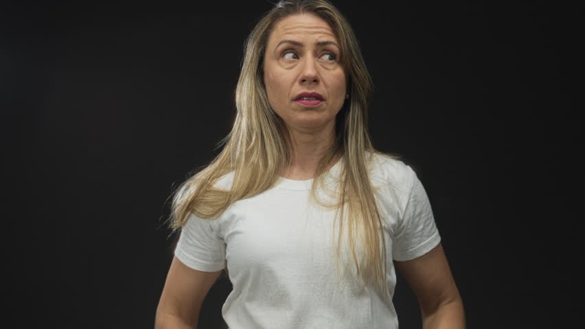 Middle age blonde woman grimaces and rolls eyes upward in black studio portrait; annoyance frustration.