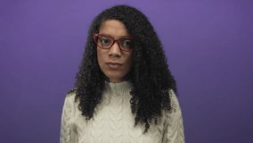Woman with curly hair wearing red glasses and cream sweater touches forehead in purple studio; stress worry anxiety tension. - Powered by Shutterstock - Get 15% off with code: PIKWIZARD15