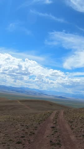 Vertical video of a car driving along a country road under blue sky. Altai desert and semi-desert environment.