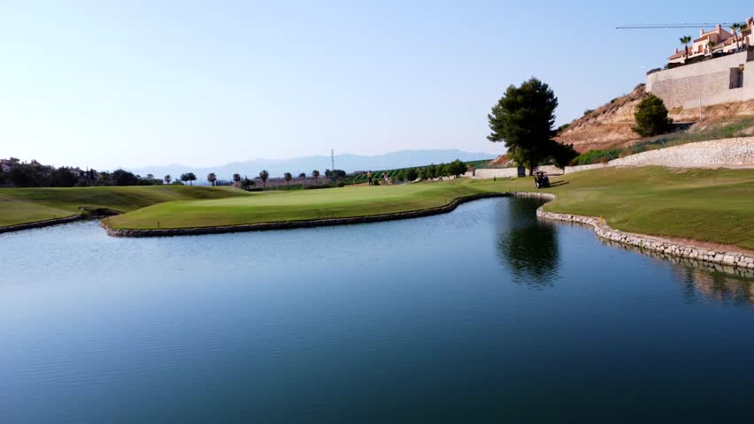 Golfers are enjoying a sunny day on a picturesque golf course, navigating a challenging water feature - Powered by Shutterstock - Get 15% off with code: PIKWIZARD15