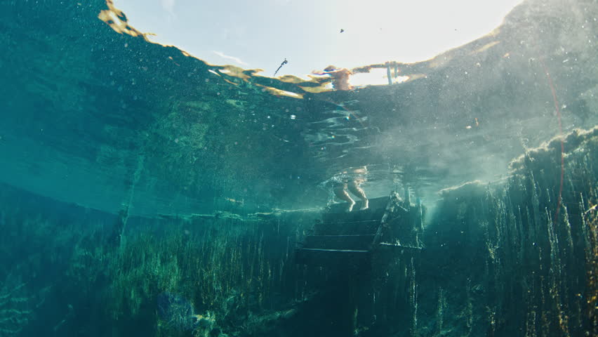 Man dives and swims underwater in an extremely crystal clear lake. Person jumps into the lake named Goluboye Ozero near the city of Samara in Russia