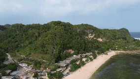 Vertical 9:16 drone footage, 2K 30fps. Aerial view of a coastal village with small houses near the beach, surrounded by dramatic cliffs and turquoise waters. Scenic tropical shoreline landscape. - Powered by Shutterstock - Get 15% off with code: PIKWIZARD15