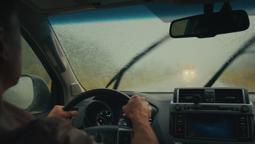 Limited visibility driving. Man steers the car on a narrow rural road during heavy rain shower with cars passing by.