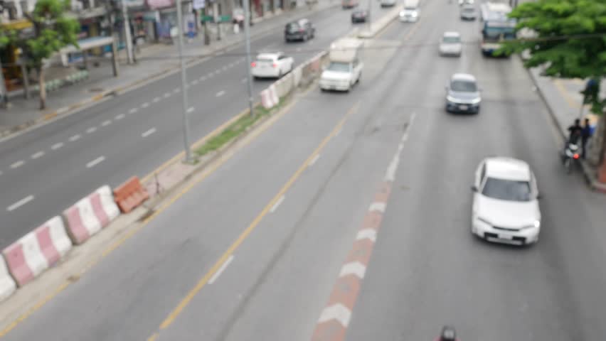 Blurred daytime view of Bangkok street with moving traffic and vehicles.